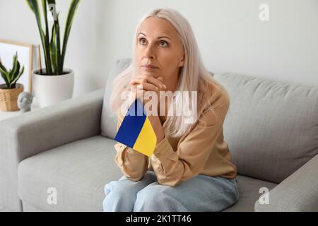 Reife Frau mit Fahne der Ukraine zu Hause beten Stockfoto