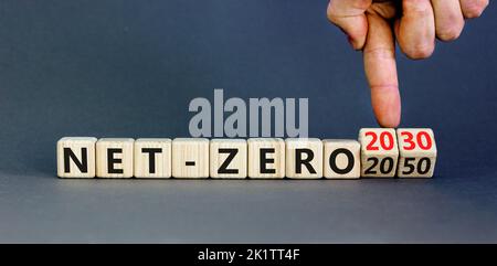 NET-Zero 2030-Symbol. Konzeptwörter Net-zero 2030 oder Net-zero 2050 auf Holzwürfeln. Geschäftsmann Hand. Schöner grauer Hintergrund. Geschäftlich, ökologisch Stockfoto