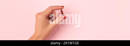 Gepflegte weibliche Hand mit winziger Flasche Softdrink auf rosa Hintergrund Stockfoto