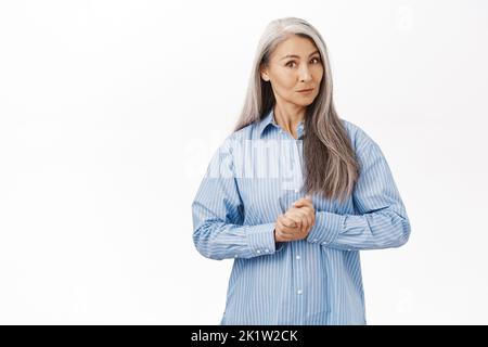 Bild von einer japanischen älteren Frau, einer schönen Dame mittleren Alters mit grauen Haaren, assistierend, bereit zu helfen, beratend, auf weißem Hintergrund stehend Stockfoto