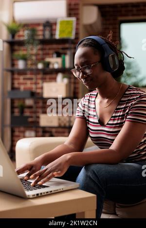 Freiberuflicher Mitarbeiter mit Kopfhörern, der an einem Laptop arbeitet und im Home Office Musik hört. Telearbeiter in Ohrhörern, Schüler, die sich Online-Lehrgänge ansehen, unterhaltsame Videos Stockfoto