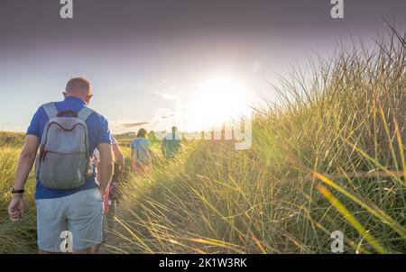 Kleine Gruppe ein Spaziergänger, der im späten Abendlicht durch die Sanddünen, Embleton, Northumberland, England, Großbritannien, einen Fußpfad entlang läuft Stockfoto