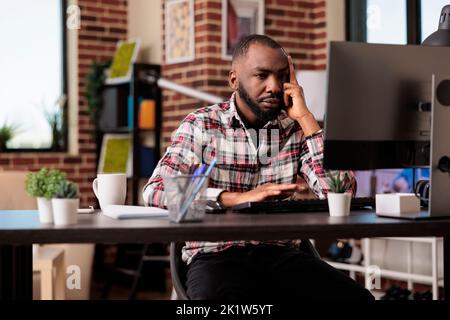afroamerikanische, müde Angestellte, die an einem Webinar teilnehmen, fühlen sich müde und frustriert über die Remote-Arbeitsbelastung am Computer. Gestresste, erschöpfte Person, die freiberuflich von zu Hause aus arbeitet und unglücklich ist. Stockfoto