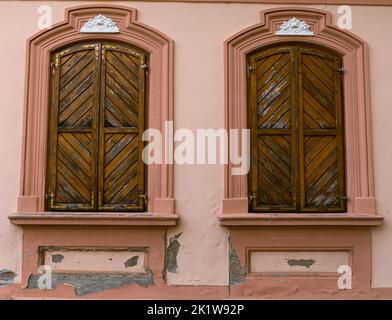 Eine Nahaufnahme von zwei Holzfenstern mit schönen Rahmen, die in einer rosa Wand platziert sind Stockfoto
