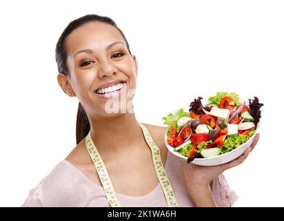 Messen und Fortschritte machen. Porträt einer attraktiven jungen Frau mit einem Maßband, das über ihren Hals drapiert und eine Schüssel Salat hält. Stockfoto