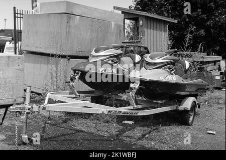 Jetskis auf einem geparkten Anhänger auf dem Parkplatz einer verlassenen Fabrik in Gloucester Harbour, Massachusetts. Das Bild wurde auf analogem Schwarz und aufgenommen Stockfoto