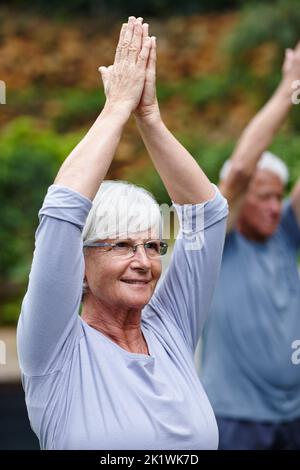 Verbesserung ihrer Gesundheit und ihres allgemeinen Wohlbefindens. Eine ältere Frau, die mit ihrem Mann im Freien Yoga macht. Stockfoto