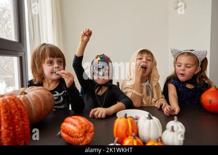 Kleine Kinder in Halloween Kostümen essen Leckereien am Tisch Stockfoto