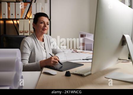 Reifere Architektin, die an einem Grafiktablett an ihrem Schreibtisch im Büro arbeitet Stockfoto