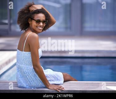 Ich würde nirgendwo anders sein wollen als hier. Voller Schuss einer attraktiven ethnischen Frau, die am Pool posiert. Stockfoto