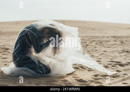 Weibliches Leid. Unschärfende Silhouette. Isolation Einsamkeit. Profil der depressiven Frau in schwarz sitzen auf den Knien umklammenden Kopf in Polyethylen-Film fliegen Stockfoto