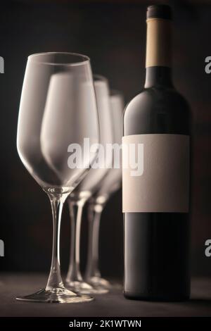 Weingläser und eine Flasche Rotwein mit weißem Etikett ohne Aufschrift. Schönes gefühlvolles Stillleben, dunkler Hintergrund atmosphärische Stimmung. Stockfoto