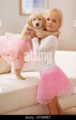 Wir sehen nicht aus wie Zwillinge. Ein kleines Mädchen, das ihren Welpen in einem Tutu kleidet. Stockfoto