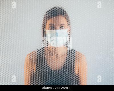 Luftverschmutzung. Unschärfes Hochformat. Atemwegserkrankung. Betroffene Frau in schützende Gesichtsmaske hinter transparenten Polyethylen Luftpolsterfolie Textur d Stockfoto