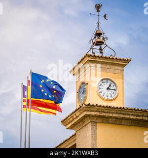Flaggen der Europäischen Union, Spaniens und der Balearen, die vor dem mediterranen Uhrturm des Regierungssitzes im Wind winken. Stockfoto