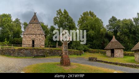 Wexford, Irland - 18. August 2022: Blick auf ein frührekonstruiertes christliches Kloster im Irish National Heritage Park mit einem großen keltischen Kreuz i Stockfoto