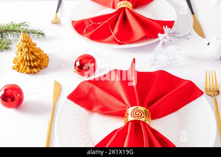 Schönes, modernes Design der Weihnachtsplatte. Rote Servietten gefaltet in einem Fächer mit Dekorationen auf weißen Tellern Stockfoto