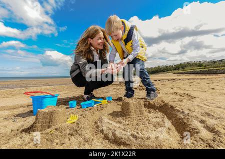 Eine Mutter mit ihrem kleinen Sohn Sandburgen am Strand bauen Stockfoto