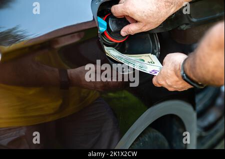 Hand of man, die Geld in den Tank des Autos, Nahaufnahme, Konzept der teuren Kraftstoff, Kraftstoff Krise steckt Stockfoto