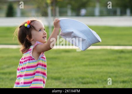 Kleinkind Baby Mädchen trägt hell gestreiften Sommer Body, nehmen Sie aus und hält ihre weiße panama Eimer Hut. Kleines Kind Kind geht im Sommer öffentliche pa Stockfoto