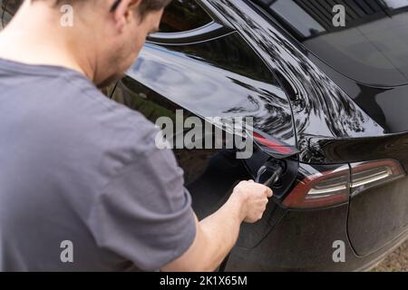 Ein Mann, der ein Elektroauto mit Elektroautos an einen Netzladegerät angeschlossen hat Stockfoto