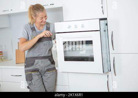 Junge Frau suchen Ofen mit Schraubendreher Stockfoto