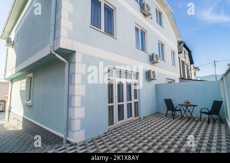 Außenansicht des Hinterhofs Moderne Villa oder Wohngebäude mit Tisch und Stühlen auf der Terrasse und Zaun.