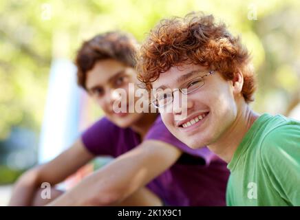 Zeit für etwas Sonnenschein. Portrait von zwei Jungen, die an einem sonnigen Tag in einem Park sitzen. Stockfoto