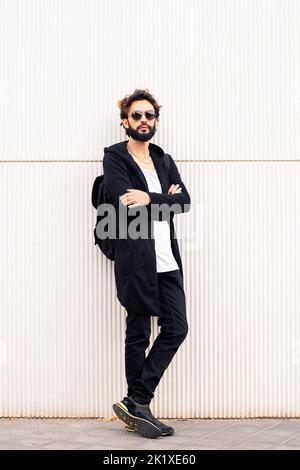 Junger Mann mit Sonnenbrille, der an einer weißen Wand gelehnt ist Stockfoto