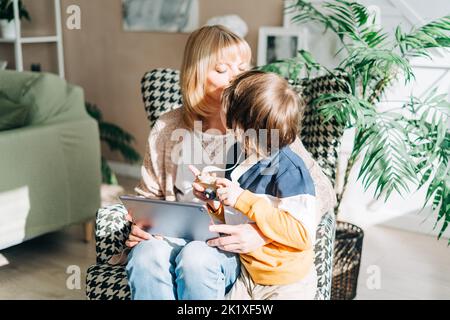 Ältere Frau und Sohn Kind spielen mit Tablet-pc. Lächelnde Frau und ihr Enkel sitzen zu Hause mit Gadget digitalen Gerät für Online-Shopping Internet Stockfoto