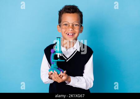 Foto von Smart positive Junge toothy Lächeln Hände halten Teleskop isoliert auf blauem Hintergrund Stockfoto