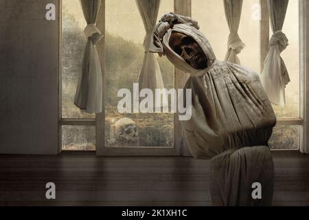 Pocong ist mit einem weißen Leinentuch bedeckt, das auf einem verlassenen Haus steht. Halloween-Konzept Stockfoto