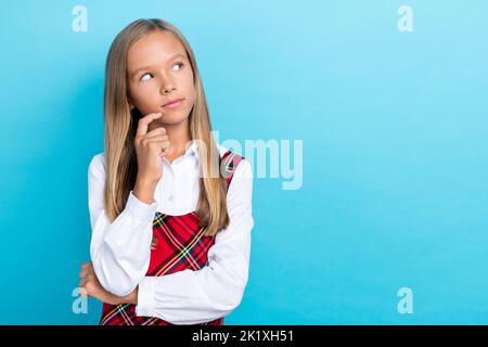 Foto von jungen niedlichen kleinen Schüler Mädchen berühren kinngesinnten Blick leeren Raum Werbung Einkaufen nachdenklich isoliert auf blauem Hintergrund Stockfoto