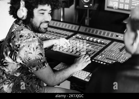 Musikproduzenten mischen neues Album im Produktionsstudio - Fokus auf Mann rechts - Schwarz-Weiß-Schnitt Stockfoto