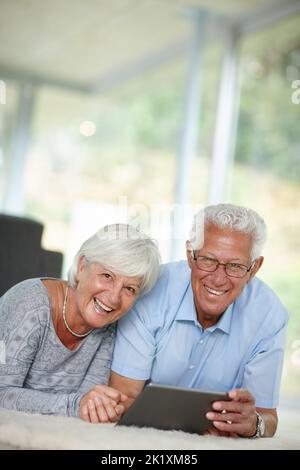 Sonntagssurfen. Ein Seniorenpaar liegt auf dem Boden, während er ein digitales Tablet benutzt. Stockfoto