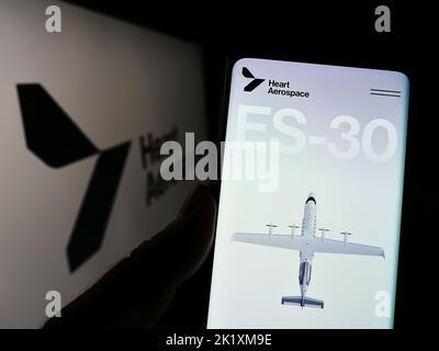 Person, die Mobiltelefon mit der Webseite des schwedischen Unternehmens Heart Aerospace ab auf dem Bildschirm vor dem Logo hält. Konzentrieren Sie sich auf die Mitte des Telefondisplays. Stockfoto