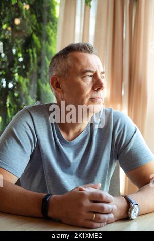 Reifer, nachdenklicher Geschäftsmann, der im Café am Tisch sitzt und auf das Fenster blickt. Schöner grauhaariger 50-jähriger Mann, der sich im Café ausruhte. Moderner Lifestyle Stockfoto