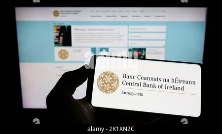 Person mit Mobiltelefon und Logo des Finanzinstituts Central Bank of Ireland auf dem Bildschirm vor der Webseite. Konzentrieren Sie sich auf die Telefonanzeige. Stockfoto