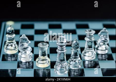 Schachfiguren aus klarem Glas, in einer Reihe angeordnet, die in einem Schachbrett aus Glas reflektiert werden. Isoliert auf Schwarz Stockfoto