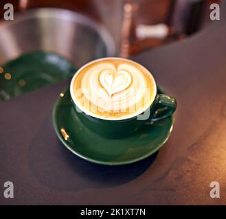 Kaffeekultur. Hochgedrehte Aufnahme einer liebevoll zubereiteten Tasse Cappuccino, die auf einem Kaffeetisch sitzt. Stockfoto