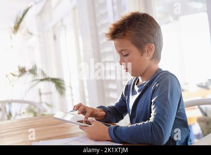 Das macht das Lernen so viel besser. Ein kleiner Junge verwendet ein digitales Tablet, um seine Hausaufgaben zu machen. Stockfoto