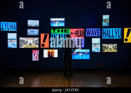 London, Großbritannien. 21. September 2022. Ein Mitarbeiter posiert mit Bildschirmen, die ein Video vom „Gangnam-Stil“ von PSY am Eingang von „Hallyu! The Korean Wave“ im V&A Museum in South Kensington, der ersten Ausstellung dieser Art, die die farbenfrohe und dynamische Populärkultur Südkoreas feiert. Die Show beginnt am 24. September bis 25. Juni 2023. Kredit: Stephen Chung / Alamy Live Nachrichten Stockfoto