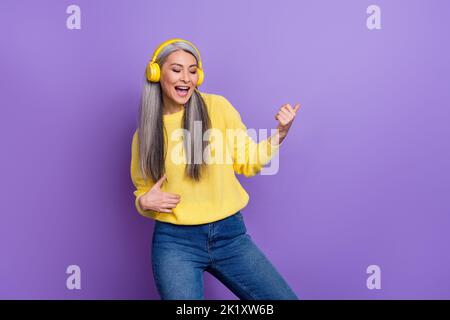 Foto von charmanten cool Dame Rentner gekleidet Pullover Kopfhörer mit Spaß spielen Gitarre isoliert lila Farbe Hintergrund Stockfoto