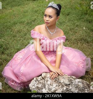 Eine philippinische Prinzessin, die ein rosa Kleid und eine Krone trägt und im Freien sitzt Stockfoto