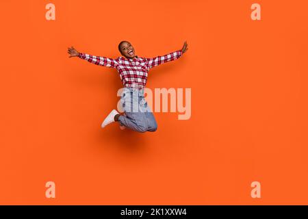 In voller Länge Foto von sorglosen aufgeregt Mädchen heben die Arme fliegen springen isoliert auf orangen Hintergrund Stockfoto