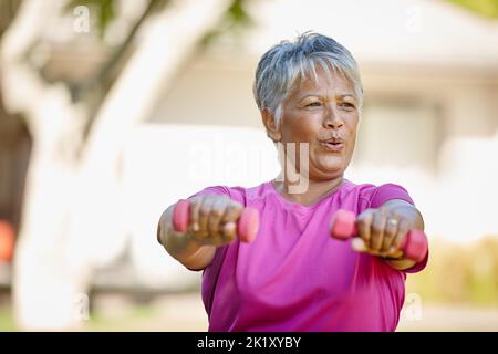 Eine reife Frau, die Hanteln nach draußen hebt. Stockfoto