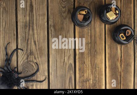 Drei kleine Hexenkessel mit verschiedenen Süßigkeiten stehen auf einem Holztisch. In der gegenüberliegenden Ecke sitzt eine Spinne Stockfoto