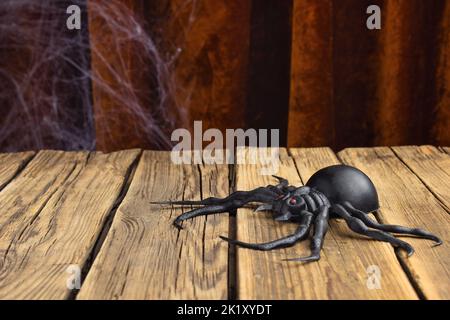 Gruselige gefälschte Spinne auf einem alten Holzbrett. Vor dem Hintergrund des Vintage-Vorhangs aus braunem Samtgewebe Stockfoto