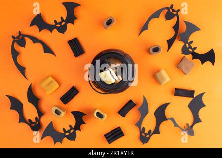 Halloween flach Lay Zusammensetzung mit Süßigkeiten, Fledermäuse und in der Mitte ist ein kleiner Kessel mit Süßigkeiten auf orangefarbenem Hintergrund. Fröhliches halloween Banner Spott Stockfoto