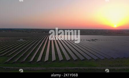 Große Sonnenkollektoren auf einer Solarfarm bei Sonnenuntergang im Sommer. Solarzellen-Kraftwerke. Footage-Video 4K, Luftdrohnenansicht Stockfoto